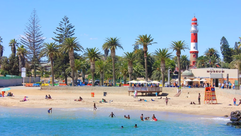People enjoying the beach at Swakopmund Mole, Namibia, with the Mole Lighthouse and Museum in the background.